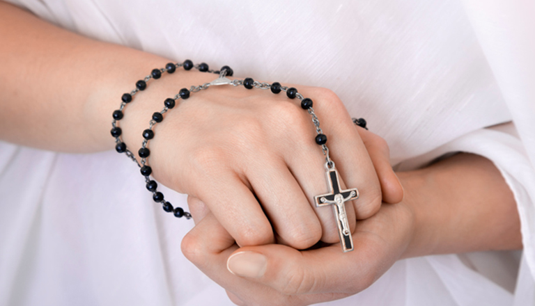 hands clasping rosary with small cross at the end