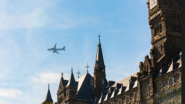 An airplane flies overhead in a clear blue sky with Healy Hall in the background