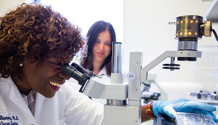 woman looks through microscope as other woman stands watching