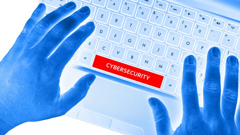 Photo negative of hand on computer keyboard that reads "Cybersecurity" on the space bar