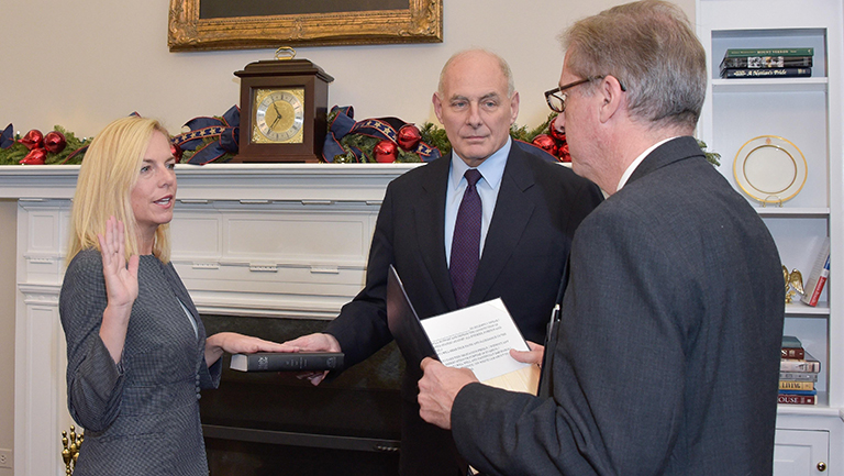 Kirstjen Nielsen with hand on bible being sworn in as new DHS head, as John Kelly and David Kalbaugh look on