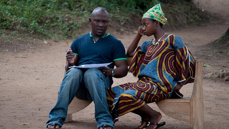 A man and a woman sit talking on a bench in Sierrra Leone