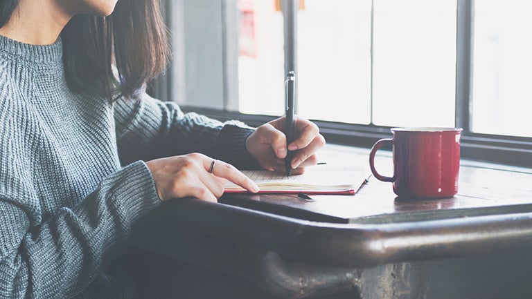 A young woman sits at a table writing 