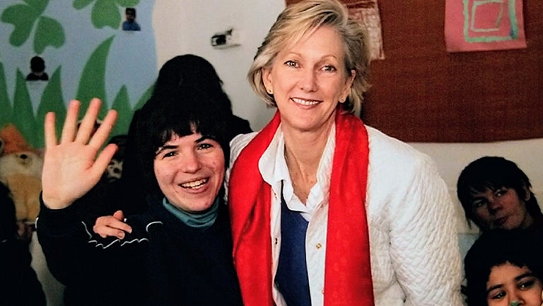 Nancy McEldowney smiling with orphan on one side of her who is waving and other children in the background