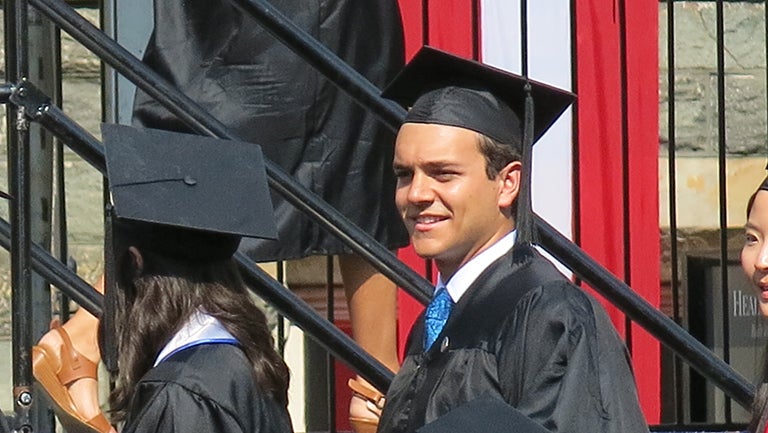 Jose Luna walks off stage near the American flag during commencement ceremony on Healy Lawn