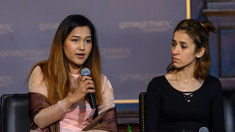 Wai Wai Nu with microphone and Nadia Murad sitting onstage in Gaston Hall