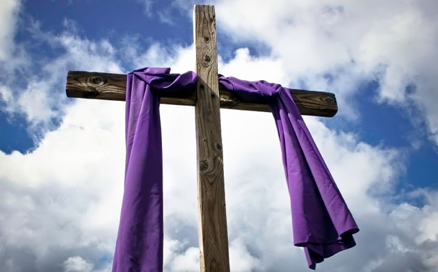 A photo of a wooden cross with a purple sash across it.