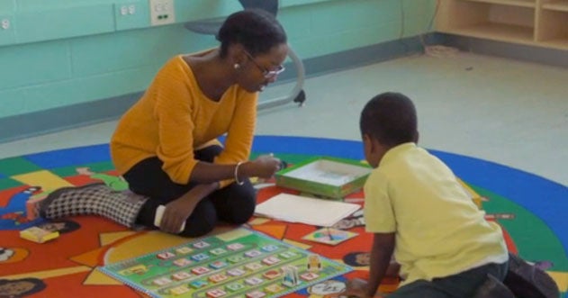 A volunteer plays with a student with letters in a classroom