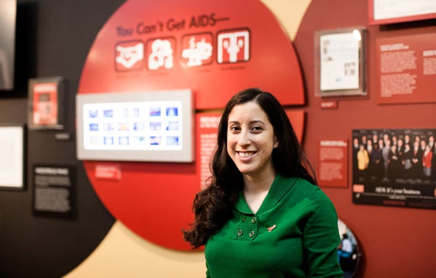 Nina Martinez stands in front of AIDS awareness posters