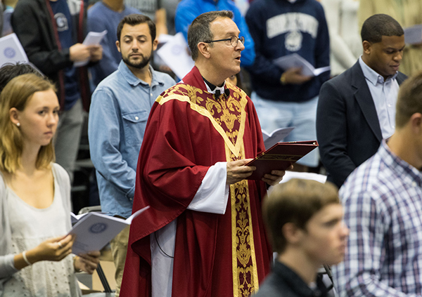 Rev. Mark Bosco, S.J., dressed in attire for Mass, stands among several students during Mass of the Holy Spirit
