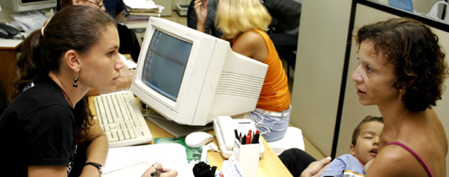 A worker at Saúde Criança sits behind a computer helping a woman and her young child