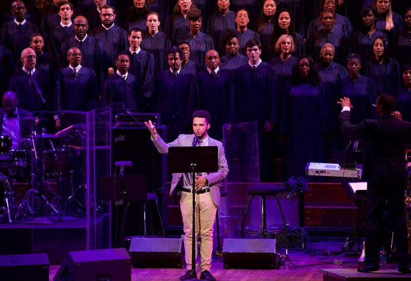 Yonas Araya speaks at a podium on stage with the Let Freedom Ring! Choir at the Kennedy Center