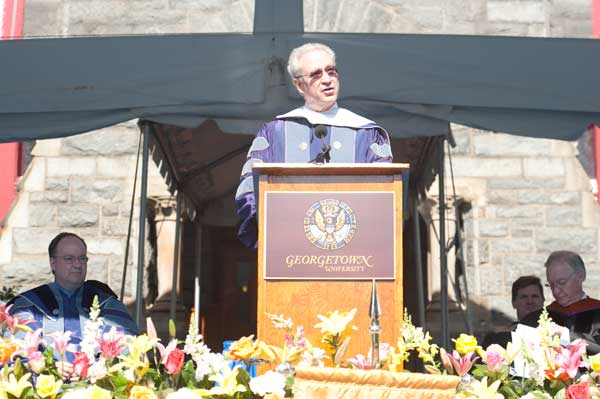 Michael C. Jensen speaks behind a podium while others look on from the stage