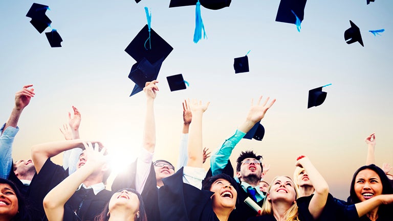 Graduates wearing gowns throw their caps into the air