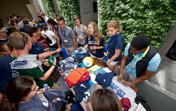 Groups of students gather around tables with t-shirts and college paraphernalia 