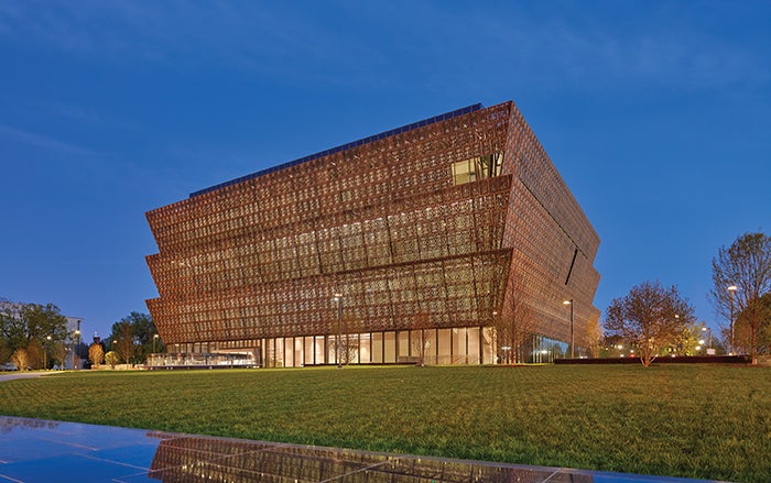 A well lit Smithsonian National Museum of African American History and Culture appears with a night blue sky behind it.