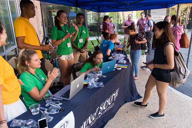 a new female student visits a table full of new student orientation team members for help during move-in