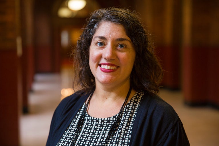 Samantha Pinto smiles into the camera with a lit hallway in the background