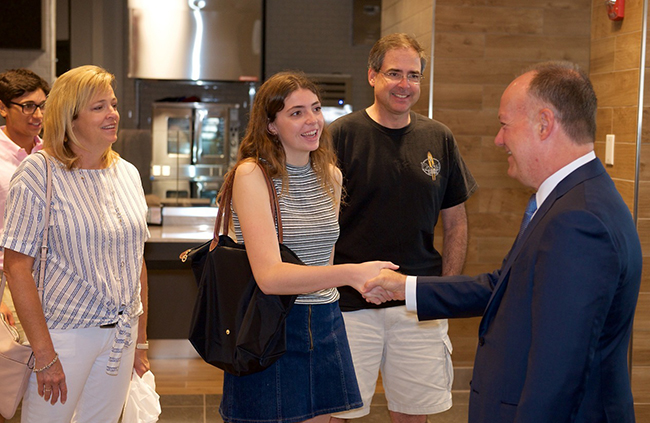 President John J. DeGioia shakes the hand of an incoming student in the dining facility while her parents look on.