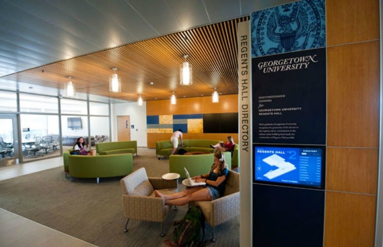 Students lounge in furniture next to a digital display with a directory for Regents Hall