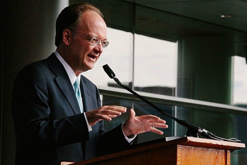 John J. DeGioia speaks behind a podium while raising his hands