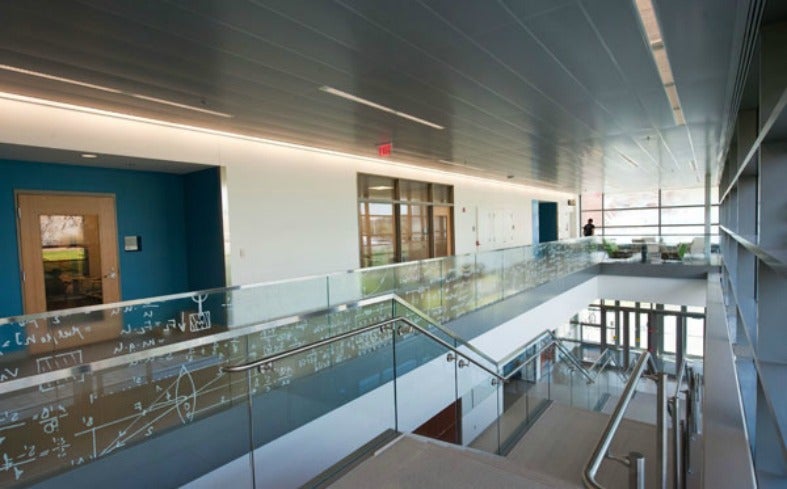 View from the top of a staircase which is lined by glass with equations written on it