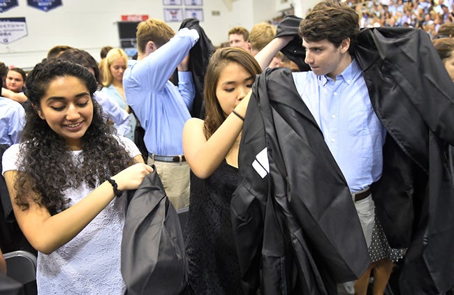 Female and male students put on black robes issued to them during New Student Convocation