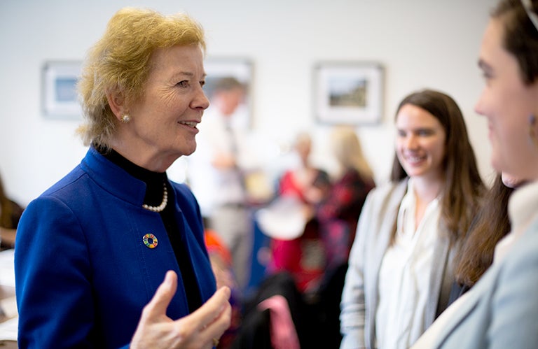 Former Irish President Mary Robinson talks to two female students inside a conference room.