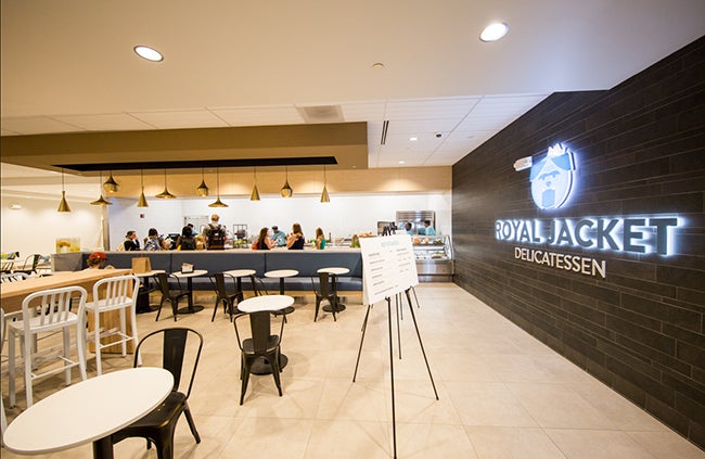 The Royal Jacket sign appears in the foreground as customers place their order at the delicatessen in the background.