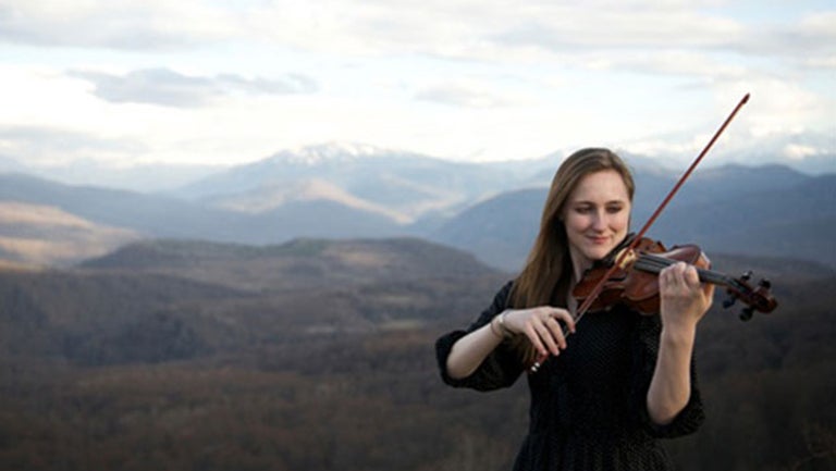 Hannah Schneider plays violin with mountains in the background.