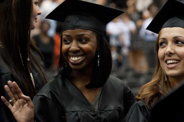 A graduate smiles and waves while another looks to the audience