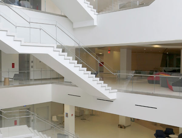 Inside the SCS campus an all white atrium with a floating staircase with glass handrails is filled with natural light