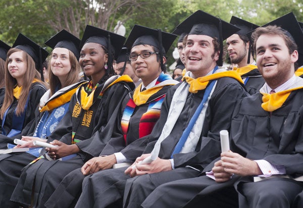 Graduates look up at the stage while smiling and holding scrolls