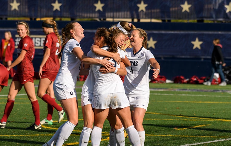 Carson Nizialek, Meaghan Nally, Kelly Ann Livingstone, Kyra Carusa embrace with excitement after a game on the soccer field.