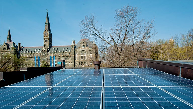 Solar panels are shown in the foreground from the rooftop of townhouse with a view of Healy Hall in the background