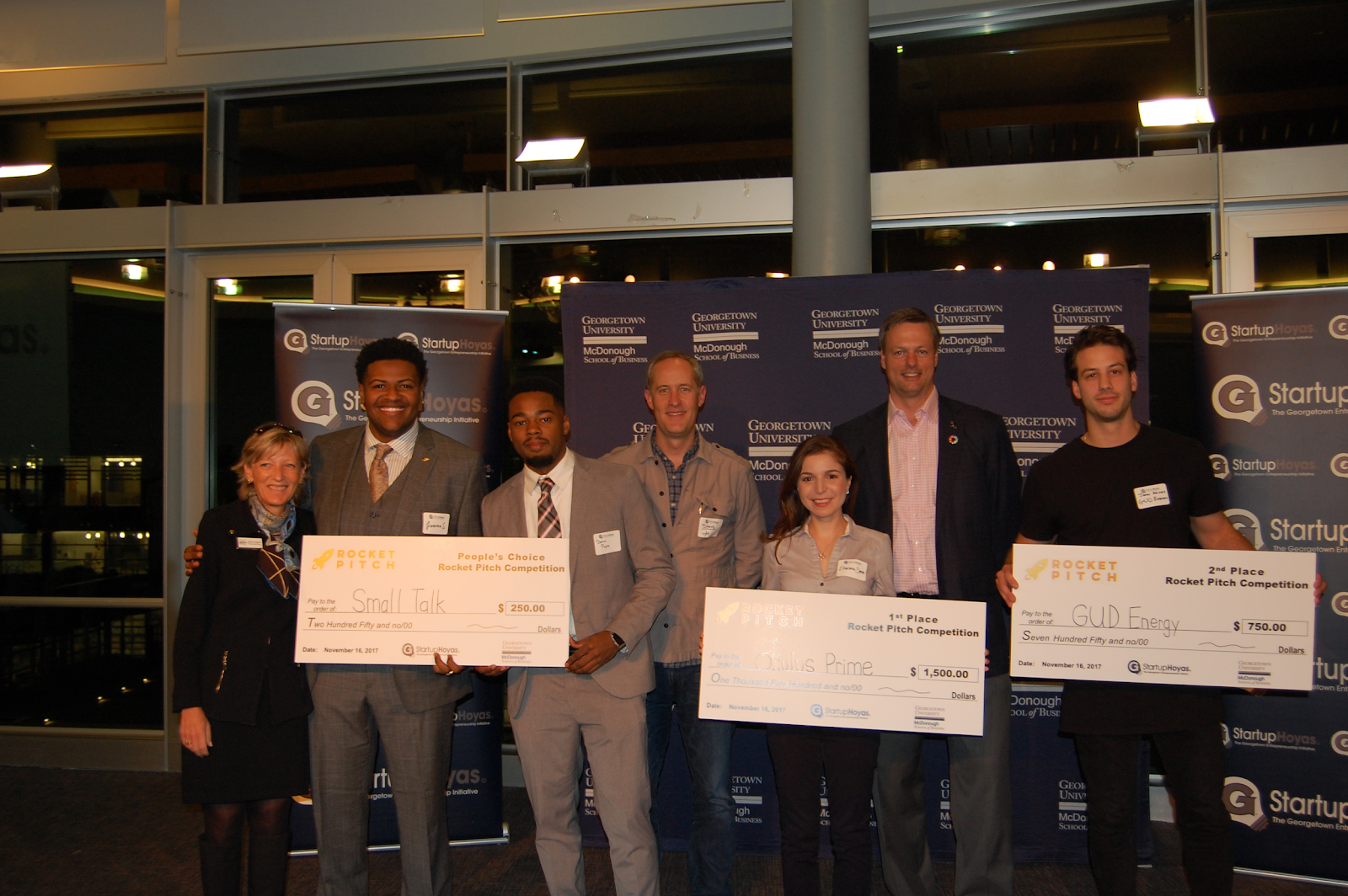 Students in Startup Hoyas hold large checks.