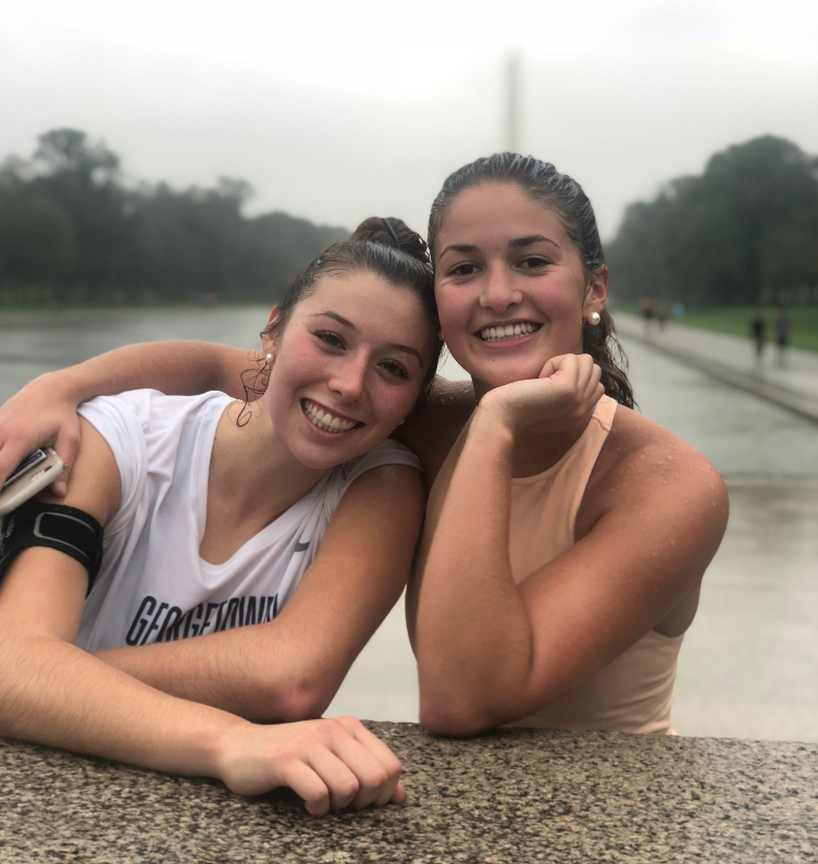 Two students smile in front of the National Monument on a rainy day