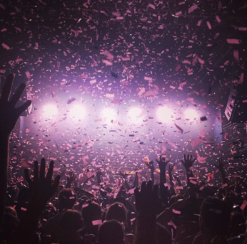 Confetti is thrown at a concert and lights illuminate the crowd