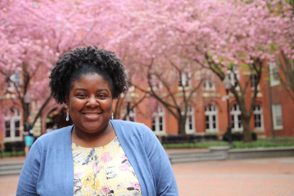 Whitney Maddox smiles for the camera in front of Cherry Blossom trees.