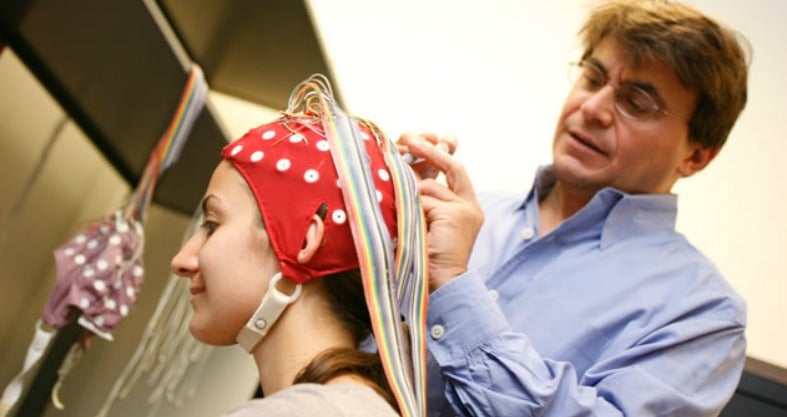 Michael Ullman attaches wires and a cap to a woman's head in a lab