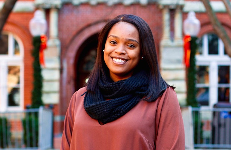 Shakera Vaughan stands outside in front of a red brick building with a smile.