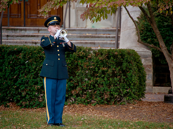 A member of the U.S. Army Band in uniform plays "Taps" on an instrument during the ceremony.