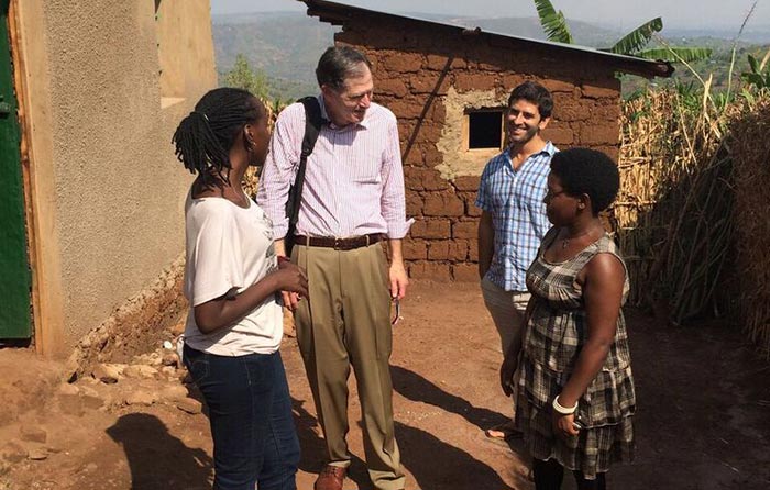 Edward Soule stands in a village talking to residents with a home in the background