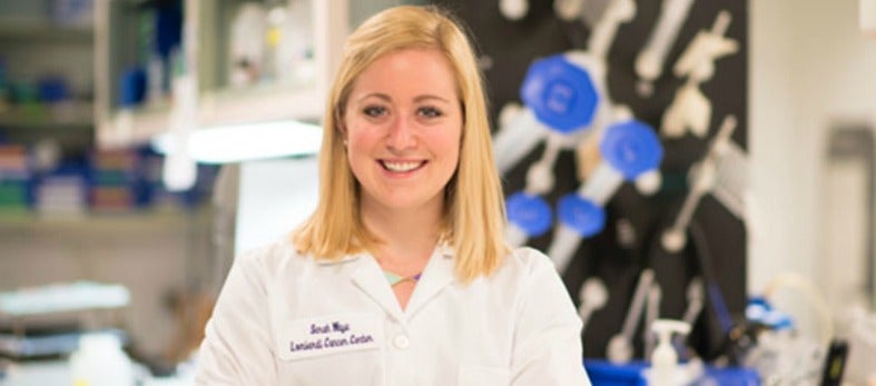 Sarah Waye in a lab, smiles and wears a lab coat