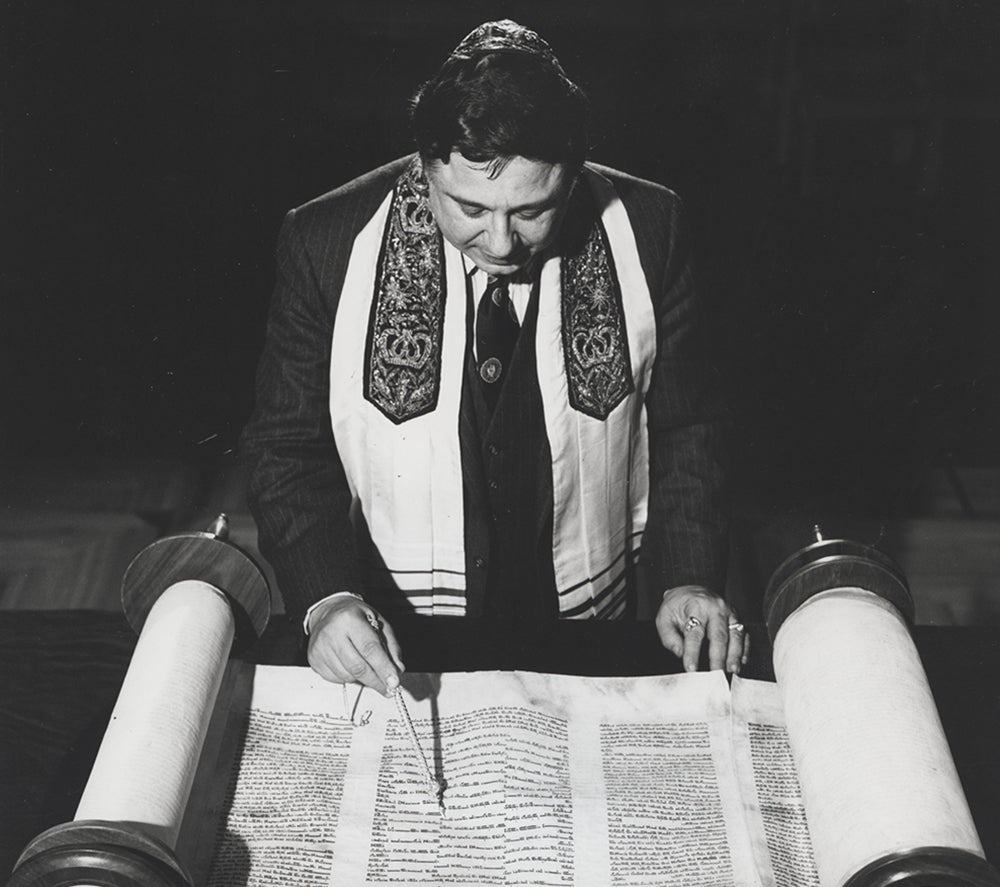 Rabbi Harold White reads over scrolls laid out on table.