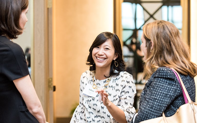 Tiffany Yu smiles into the camera while talking to two other women facing her on each side.